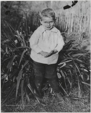 Meador as a toddler stands by a large plant.