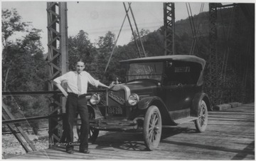 The unidentified man poses beside a car on top of the newly completed bridge over the mouth of the Bluestone River. 