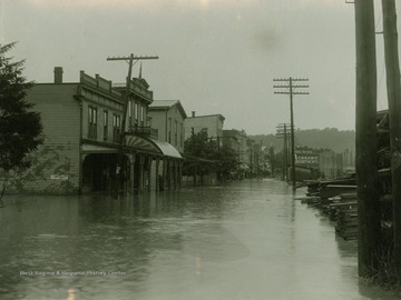 Water levels are high enough that they reached the front decks of most of the buildings lining the street. Cream of Kentucky sign can be seen in background.