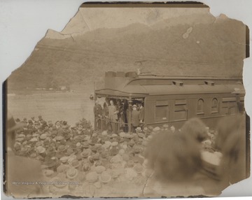Davis, from Clarksburg, W. Va., is pictured front and center standing on a train car and addressing the large crowd gathered before him. On the far left, also on the train with Davis, is James Rushford. Remaining subjects are unidentified. 