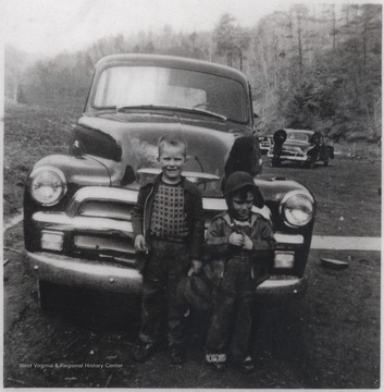 Cecil Meador's sons, Nanes and unknown, pose in front of a parked car. 