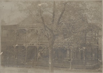 An unidentified woman sits on the ledge of the ground floor porch. The site of the pictured home is now where a Methodist Church sits today.