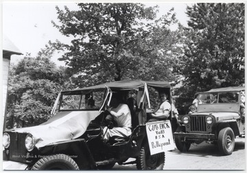 Jeeps filled with boy scouts head down Ballengee Street to participate in the parade. To the left is Carnagie Library. 