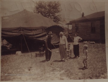 Two men, a woman and a child stand outside the large tent set up for movie watching. Subjects unidentified.