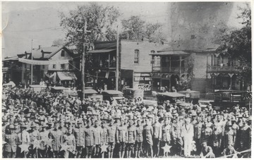 A large group of uniformed soldiers pose together behind decorations. In the background is Second Avenue and Temple Street. Subjects unidentified.
