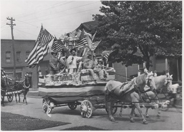 A Palace Clothing Co. parade float decorated in American flags is drawn by two horses. 