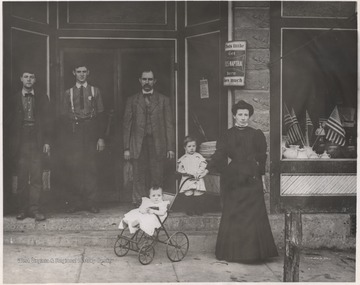 A woman and her children stand outside of the building beside three men. The building is located on Third Avenue. A sign on the entrance-way advertises Fels-Naptha soap. Subjects unidentified. 