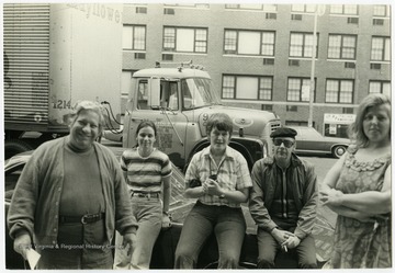 Maryat Lee and a group sit outside on the street likely in New York.Maryat Lee (born Mary Attaway Lee; May 26, 1923 – September 18, 1989) was an American playwright and theatre director who made important contributions to post-World War II avant-garde theatre.  She pioneered street theatre in Harlem, and later founded EcoTheater in West Virginia, a community based theater project.Early in her career, Lee wrote and produced plays in New York City, including the street play “DOPE!”  While in New York she also formed the Soul and Latin Theater (SALT), and wrote plays centered around the lives of the actors in the group.In 1970 Lee moved to West Virginia and formed the community theater group EcoTheater in 1975.  Beginning with local teenagers from the Governor’s Summer Youth Program, the rural theater group grew, and produced plays based on oral histories collected from the local community.  Each performance of an EcoTheater play involved audience participation and discussion.  With the assistance of the Humanities Foundation of West Virginia, guest scholars became a part of EcoTheater.