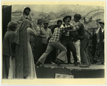 In this performance of "John Henry" the Governor's Summer Youth Program participants are the actors. The three actors in the fight were neighbors of Maryat Lee's at Powley Creek near Hinton, W. Va.. Their names were Randy and Mike Buckland, and Benny Allen.Maryat Lee (born Mary Attaway Lee; May 26, 1923 – September 18, 1989) was an American playwright and theatre director who made important contributions to post-World War II avant-garde theatre.  She pioneered street theatre in Harlem, and later founded EcoTheater in West Virginia, a community based theater project.Early in her career, Lee wrote and produced plays in New York City, including the street play “DOPE!”  While in New York she also formed the Soul and Latin Theater (SALT), and wrote plays centered around the lives of the actors in the group.In 1970 Lee moved to West Virginia and formed the community theater group EcoTheater in 1975.  Beginning with local teenagers from the Governor’s Summer Youth Program, the rural theater group grew, and produced plays based on oral histories collected from the local community.  Each performance of an EcoTheater play involved audience participation and discussion.  With the assistance of the Humanities Foundation of West Virginia, guest scholars became a part of EcoTheater.