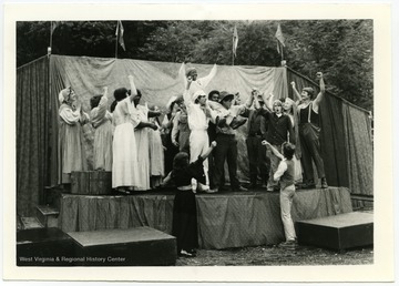 "John Henry being triumphantly born away.  Governor's Summer Youth performers in EcoTheater."  This scene is from the play "John Henry: A Drama with Music" by Maryat Lee.  The Governor's Summer Youth include Kathy Jackson who performed as John Henry (Jackson is wearing overalls in the background.)Maryat Lee (born Mary Attaway Lee; May 26, 1923 – September 18, 1989) was an American playwright and theatre director who made important contributions to post-World War II avant-garde theatre.  She pioneered street theatre in Harlem, and later founded EcoTheater in West Virginia, a community based theater project.Early in her career, Lee wrote and produced plays in New York City, including the street play “DOPE!”  While in New York she also formed the Soul and Latin Theater (SALT), and wrote plays centered around the lives of the actors in the group.In 1970 Lee moved to West Virginia and formed the community theater group EcoTheater in 1975.  Beginning with local teenagers from the Governor’s Summer Youth Program, the rural theater group grew, and produced plays based on oral histories collected from the local community.  Each performance of an EcoTheater play involved audience participation and discussion.  With the assistance of the Humanities Foundation of West Virginia, guest scholars became a part of EcoTheater.
