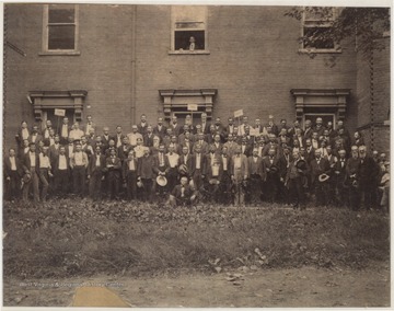 A large group of men pose beside the building with signs. Subjects unidentified.