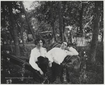 The Murrells are pictured somewhere in Summers County on a hammock resting between trees. In the background, multiple horse-drawn carriages are pictured. 