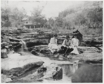 Bob Murrell busies himself by placing sticks into the water while his wife, seated on the right, watches. 