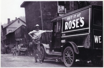 An unidentified man stands beside the old automobile that reads, "Get it at Rose's."