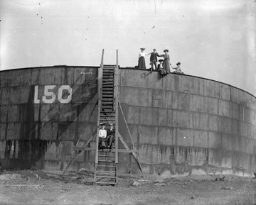 Unidentified men and women pose for portrait while standing on an oil storage tank in Morgantown, W. Va.