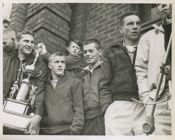 Jerry West, pictured holding the trophy, is outside of East Bank High School after leading his team to championship victory. West was the team's starting small forward. He was named All-State from 1953–56, then All-American in 1956 when he was West Virginia Player of the Year, becoming the state's first high-school player to score more than 900 points in a season.