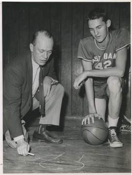 West, right, is pictured with East Bank coach Roy Williams, who is stressing defense techniques. West was the team's starting small forward. He was named All-State from 1953–56, then All-American in 1956 when he was West Virginia Player of the Year, becoming the state's first high-school player to score more than 900 points in a season.