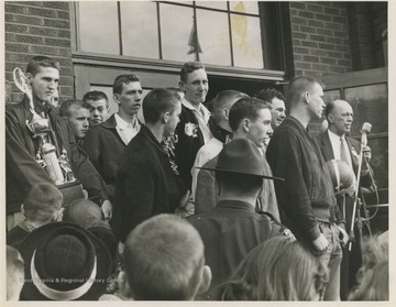 Jerry West, pictured on the left holding a trophy, is outside of East Bank High School after leading his team to championship victory. West was the team's starting small forward. He was named All-State from 1953–56, then All-American in 1956 when he was West Virginia Player of the Year, becoming the state's first high-school player to score more than 900 points in a season.