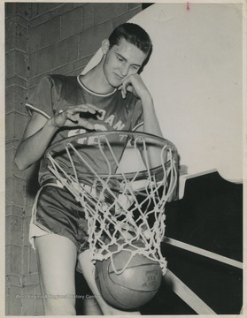 West is pictured throwing a basketball through the basket nonchalantly. He was East Bank High School's small starting forward.West was named All-State from 1953–56, then All-American in 1956 when he was West Virginia Player of the Year, becoming the state's first high-school player to score more than 900 points in a season
