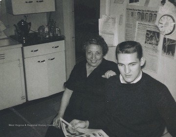 Erlinda Dinardi, sister of Ann Dinardi, and basketball star West are pictured in the Dinardi sisters' kitchen reading a newspaper.West described Ann Dinardi as his "mom away from home." She had a special relationship with many of the basketball players because she lived steps away from the Old Field House.  Her home was on Beechurst Avenue. 
