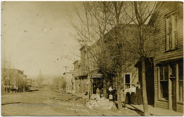 The Wayne Spiggle House is located where the Worden Restaurant sign is hanging. The subjects standing along the sidewalk are unidentified.This image is part of the Thompson Family of Canaan Valley Collection. The Thompson family played a large role in the timber industry of Tucker County during the 1800s, and later prospered in the region as farmers, business owners, and prominent members of the Canaan Valley community.
