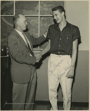 Jerry West, right, shakes hands with Coach Williams, left.West led the East Bank High School basketball team to its first ever state championship victory as its starting small forward. He was named All-State from 1953–56, then All-American in 1956 when he was West Virginia Player of the Year, becoming the state's first high-school player to score more than 900 points in a season.West was born in Cheylan, W. Va. in 1938. After high school, he went on to play basketball for West Virginia University and then rose to fame as a player for the Los Angeles Lakers of the NBA before becoming a basketball coach and manager. 