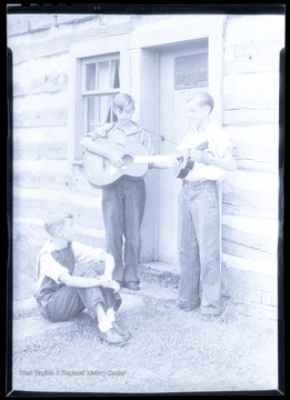 A boy watches as his two companions play their string instruments. Subjects unidentified. 
