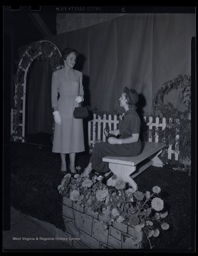 Two fashionably dressed women converse on stage. Subjects unidentified. 