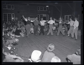 A group of men hold hands and dance around the room at the leadership conference in the State 4-H Camp. Subjects unidentified. 