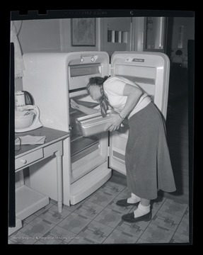 An unidentified woman inspects a refrigerator. 