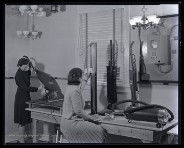 Two unidentified women study the vacuum machinery in front of them. 