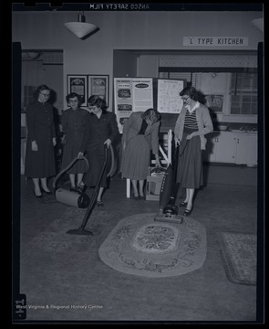 A group of women practice cleaning with vacuum cleaning machines. Subjects unidentified. 