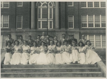 A group of male and female students pose together on the steps outside of the high school building. Subjects unidentified.