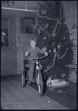 Miller Murrell on a bike next to the family Christmas tree in the basement of their home at 309 Ballengee Street, Hinton, W. Va.