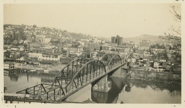 View of downtown Morgantown from across the Monongahela River bridge.  Several buildings have visible company names painted onto them.