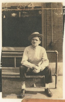 A man sitting on a rail outside The Big 4 Drug Store, located on the corner of 3rd Avenue and Temple Street, in Hinton, W. Va.  A membership card identifies B. O. Pettrie, Jr. as President of The Rail Club.
