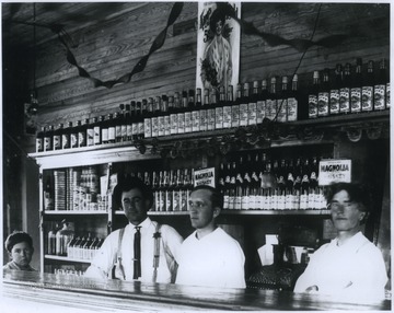 Three men and a young boy are pictured behind the bar. In the background, Magnolia Whiskey is shelved and advertised. 