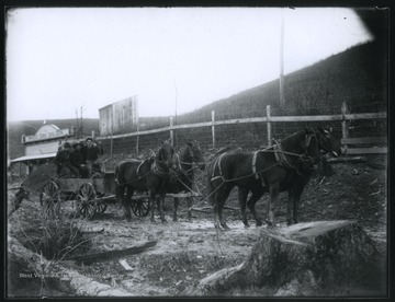 Four horses pull a cart of three men from the saloon, which is pictured in the background on the left. . 