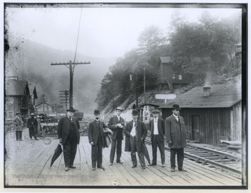 From left to right are C. C. Beury, unidentified, C. L. Garvin, Sr., Paddy Ryan, unidentified, and unidentified. The men are coal operators and are posing on the south side of the train platform.