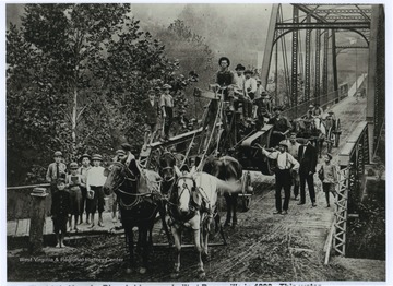 Water well drilling equipment, owned by Tom Fletcher, who is pictured standing beside the rig with the white shirt and suspenders, is being pulled across the bridge by horses. Charles E. Crutchfield has the reins. In the suit and bow tie is Anson Wade, a teacher. The bridge was built in 1893. 