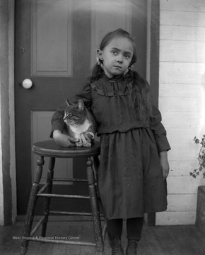 A young, unidentified girl and her cat pose on a home porch. 