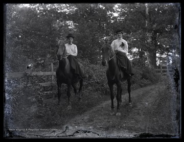 Two unidentified women riding sidesaddle along a dirt road. 