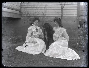 Two unidentified women sit with their pet dog on a lawn. 