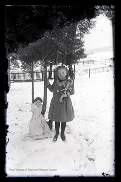 A young girl poses with her dolls outside in the snow.