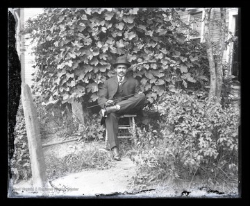 An African-American man sits with his legs crossed on a chair in a home garden. Subject unidentified. 