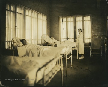 A nurse checks on a patient. The photograph shows two patients in bed. 