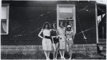Four women pose outside of a house. Two of the are in bathing suits. Subjects unidentified. 