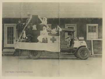 Men in military uniforms and women in nurses uniforms sit on the truck bed of a vehicle sporting the Red Cross logo. 