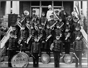 A group of unidentified boys pose in front of a building, wearing marching band uniforms and holding instruments. 