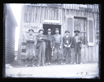 Workmen pose in front of a Franklin, W. Va. building.  The building has several signs on it, including one for Bickford & Huffman Grain Drills.  The men are likely blacksmiths.